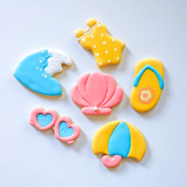 Colorful beach-themed cookies, including a wave, swimsuit, shell, flip-flops, and hearts.