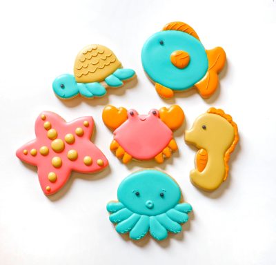 Colorful sea-themed cookies in shapes of a starfish, turtle, fish, crab, seahorse, and octopus.